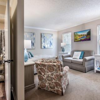 A cozy living room with modern decor, featuring a sofa and armchair, adorned with artwork and ample natural light.