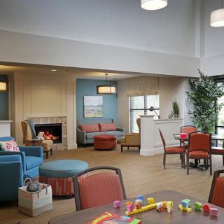 A cozy living room with modern furniture and a fireplace, featuring a seating area and children's toys.
