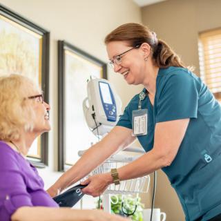A nurse smiles while checking the blood pressure of an elderly patient in a healthcare setting.