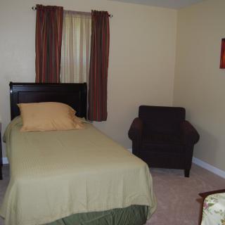 A cozy bedroom featuring a single bed and an armchair next to a window with curtains.
