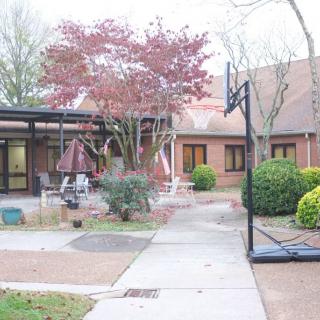 A quiet courtyard with a basketball hoop, surrounded by a brick building and lush trees.