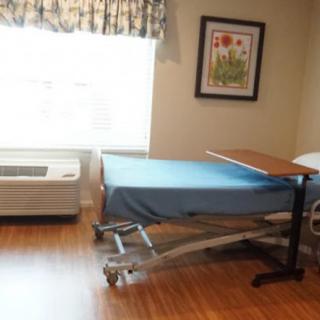 An empty hospital room featuring a single bed with blue sheets and a side table.