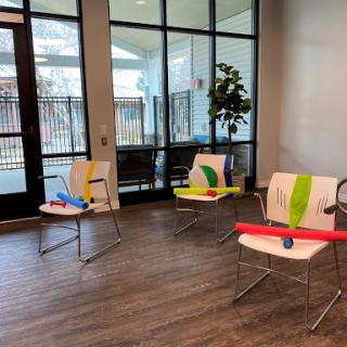 A setup for a fitness class featuring chairs with exercise bands and pool noodles in a bright indoor environment.