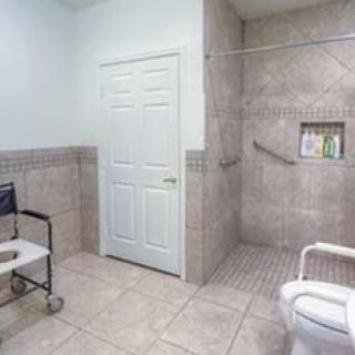 An accessible bathroom featuring a wheelchair, shower area with grab bars, and tiled walls.