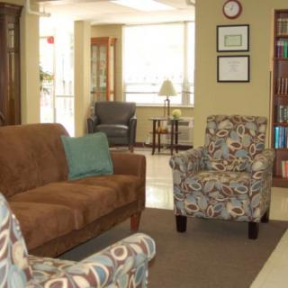 A cozy living room with a sofa, patterned armchairs, and a bookshelf.