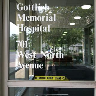 Glass entrance of Gottlieb Memorial Hospital displaying its address.
