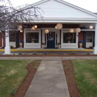 A welcoming building entrance with a pathway leading to the porch, flanked by well-maintained landscaping and lit by decorative outdoor lamps.