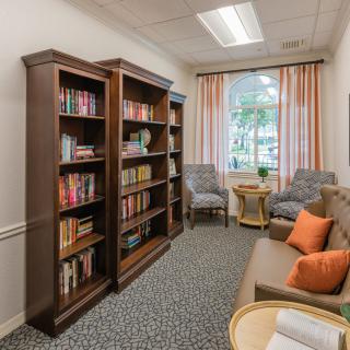 A cozy reading room featuring bookshelves filled with books, comfortable seating, and a large window with curtains.