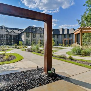 A modern residential complex with landscaped gardens and pathways under a clear blue sky.