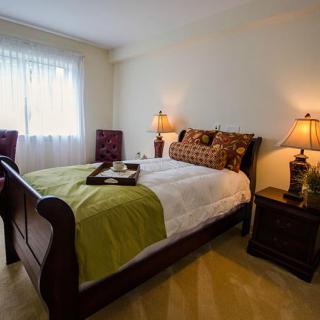 A cozy bedroom with a neatly made bed, two lamps on nightstands, and natural light coming through the window.