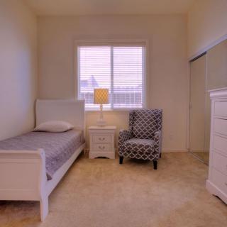 A minimalist bedroom featuring a single bed, an armchair, and a nightstand with a lamp.