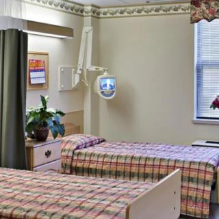 A hospital room with two beds, curtains, and a window with plants on the table.