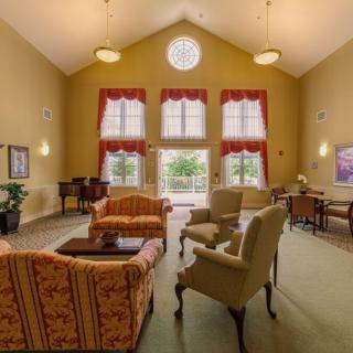 A spacious living room with high ceilings, featuring comfortable armchairs and a sofa, framed by large windows.