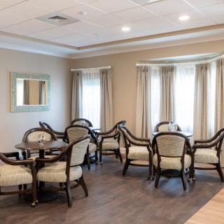 A cozy dining area with elegant chairs and tables, featuring large windows with curtains and a mirror on the wall.