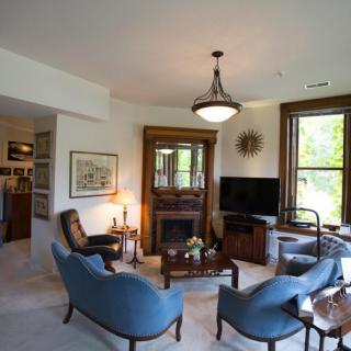 A cozy living room with blue chairs, a fireplace, and large windows offering natural light.