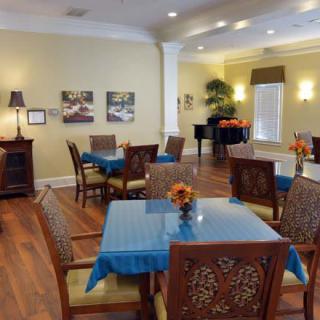 A well-lit dining room with wooden floors and neatly arranged tables and chairs.