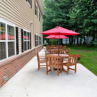 A cozy outdoor patio area featuring a wooden table and chairs, shaded by a vibrant red umbrella.