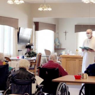 A priest conducts a religious service for elderly residents in a nursing home setting.