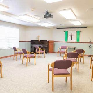 An empty church meeting room with chairs arranged in a circle, featuring a cross and green banners on the wall.