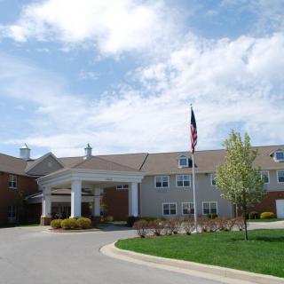 A view of a building with an entrance, landscaped grounds, and a flagpole under a partly cloudy sky.