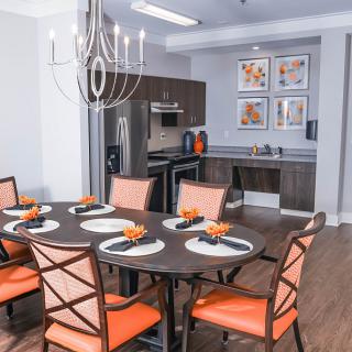 A modern dining area with a stylish chandelier, featuring orange-accented chairs and place settings.