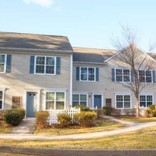 A row of suburban townhouses with a sidewalk and trees.