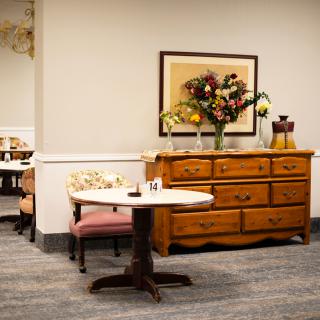 A cozy interior with a wooden dresser and small table adorned with flowers.