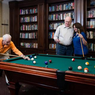 A group of people enjoying a game of billiards in a room with bookshelves.