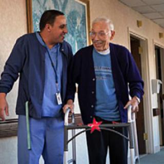 A caregiver assists an elderly man with a walker, fostering a supportive environment in a healthcare setting.