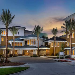 A modern residential building at dusk with palm trees lining the entrance.
