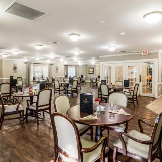 A spacious dining room with elegantly arranged tables and chairs, featuring warm lighting.