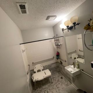 An accessible bathroom with safety features including a shower chair and grab bars.