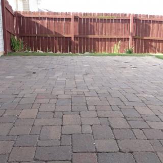 A backyard patio area with stone pavers and a wooden fence.