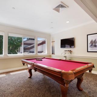 A well-lit game room featuring a pool table with a red felt top and a wall-mounted television.