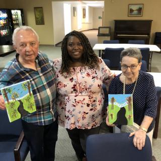 Three people smiling and holding up their paintings indoors.
