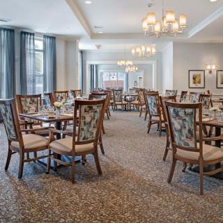 A spacious dining area with elegantly arranged tables and chairs, featuring classic chandeliers and tasteful decor.