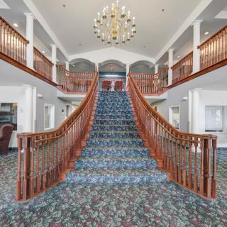 A grand, carpeted staircase with wooden railings and a large chandelier in an elegant interior setting.