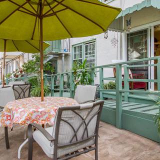 A cozy outdoor patio setup with a table and chairs under a green umbrella, surrounded by greenery.