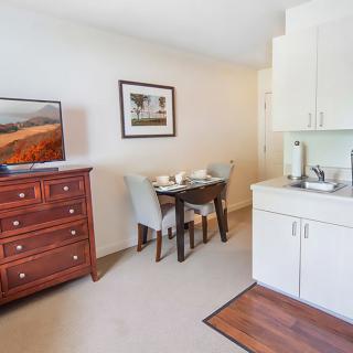 A cozy room featuring a television on a dresser, a small dining table with chairs, and a kitchenette area.