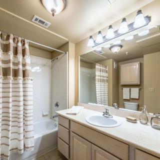 A modern bathroom featuring a sink with an illuminated mirror, bathtub with a striped shower curtain, and ample cabinet space.