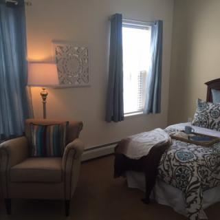 A cozy bedroom with a neatly made bed, soft lighting from an elegant lamp, and comfortable seating next to a window.