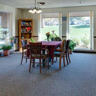 Cozy dining area with a table surrounded by chairs, large windows, and a bookshelf.
