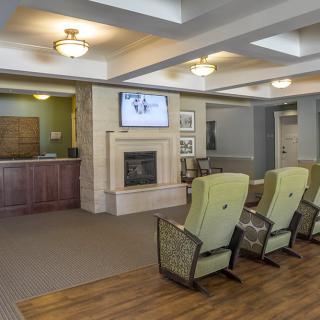 A comfortable lounge area with a row of chairs facing a fireplace and a television, adjacent to a reception desk.
