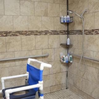 An accessible bathroom with a walk-in shower featuring a shower chair and grab bars for safety.