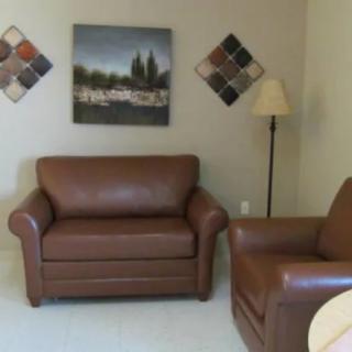 A cozy living room with brown leather chairs and wall art.