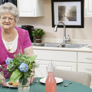 An elderly woman smiles as she prepares to serve a meal in her cozy kitchen.