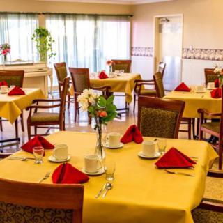 A cozy restaurant dining room with neatly arranged tables, each set with yellow tablecloths, red napkins, and floral centerpieces.
