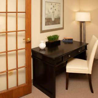 A cozy home office setup with a dark wood desk, comfortable chair, and ambient lighting.
