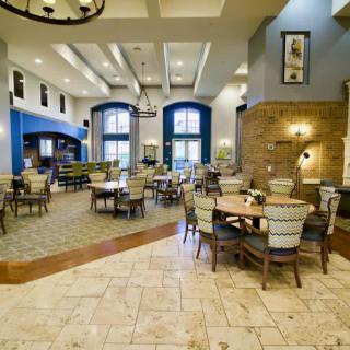 A modern and spacious dining area with large windows, elegant chandeliers, and neatly arranged tables and chairs.