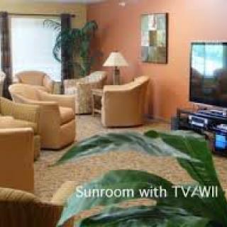A cozy sunroom featuring comfortable seating and a TV.